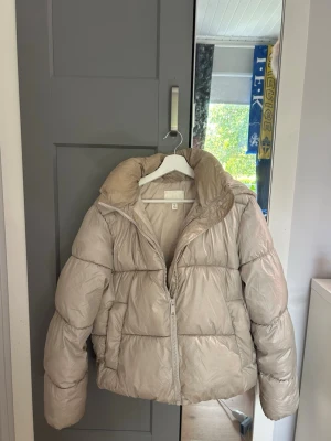 Beige pufferjacka med huva - Säljer en beige pufferjacka, väldigt bra skick förutom att den e ganska missfärgad vid huvan, perfekt till en kall vinterdag, köpt för ca 399kr❤️