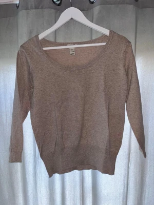 Beige tröja från H&M med rund hals - En enkel och stilren beige tröja från H&M med rund halsringning och långa ärmar. Tröjan är tillverkad i ett mjukt och tunt material, perfekt för lager på lager eller som den är. Passar till många olika stilar och tillfällen.