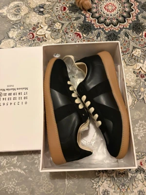 Svarta sneakers med beige sula - Snygga svarta sneakers med beige gummisula och vita skosnören. Ovandelen är i en mix av läder och mocka för en stilren look. Klassisk siluett som passar till många outfits och ger en clean vibe.