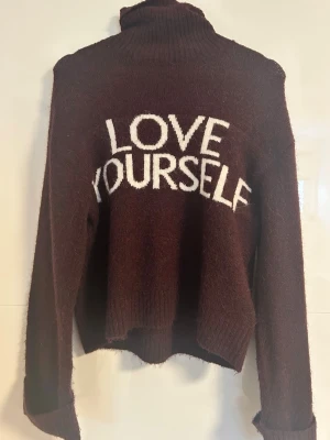 Vinröd polotröja med text - Mysig vinröd stickad polotröja med vit text 'LOVE YOURSELF' på framsidan. Tröjan har långa ärmar, hög krage och är tillverkad i ett fluffigt, mjukt material. Perfekt för kalla dagar och en avslappnad stil. Jätte mysig och endast använd 1 gång💓 passar mig som brukar ha S 