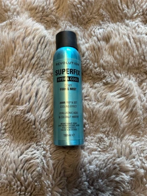 Revolution Superfix Hydra Cool Face Mist - Fräsch ansiktsmist från Revolution i metallicblå sprayflaska. Superfix Hydra Cool Dewy Fixing Mist ger en svalkande känsla och håller sminket på plats i 24 timmar. Innehåller hyaluronsyra och kokosvatten för extra återfuktning. Volym: 150 ml.