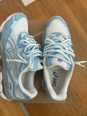  Nya oandvända Asics nyc gel sneakers  - Snygga Asics sneakers i ljusblått och vitt med mesh och mockadetaljer. Skorna har vita snören, tydlig Asics-logga på sidan och en chunky vit sula. Perfekta för dig som gillar sportig och trendig stil. Ordpris  1900-2300kr 
