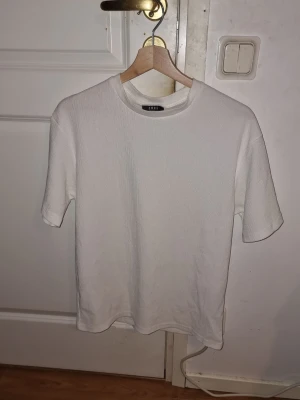 Vit t-shirt från New Yorker - En stilren vit t-shirt från New Yorker med rund hals och korta ärmar. T-shirten är gjord i ett mjukt bomullstyg och har en enkel, clean look som passar till allt. Perfekt för dig som gillar minimalistisk stil. 