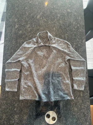 Gråmelerad långärmad tröja - En stilren gråmelerad långärmad tröja med hög krage och halv dragkedja framtill. Tröjan har en avslappnad passform och är tillverkad i ett mjukt, tunt material som passar perfekt för lager-på-lager. Enkel och clean design utan synliga loggor.