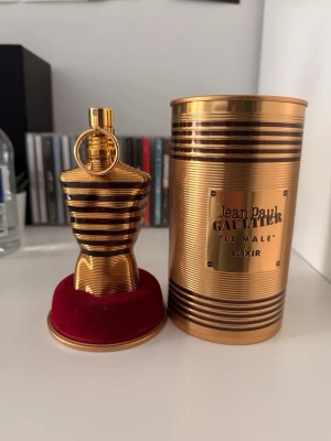Jean Paul Gaultier Le Male Elixir - Exklusiv parfymflaska i guld med svarta ränder från Jean Paul Gaultier, modell Le Male Elixir. Flaskan har en unik kroppsliknande form och levereras i en matchande guldfärgad metalltub med märkets logotyp. Perfekt för dig som gillar lyxiga och iögonfallande dofter. Cirka 50ml kvar
