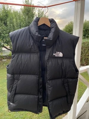 The North Face 700 dunväst svart strl L - Snygg svart 700 dunväst från The North Face med hög krage och dragkedja framtill. Västen har två sidofickor och logga på bröstet. Klassisk och stilren design som passar till det mesta. Säljes pga fel storlek. Nypris: 3099 kr
