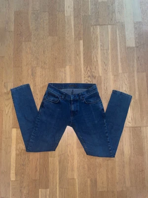 Mörkblå Nudie Jeans - Säljer ett par mörkblå jeans från Nudie med klassisk femficksdesign. Jeansen har normal midja och är tillverkade i ett mjukt denimtyg. Perfekta för en avslappnad och stilren look.