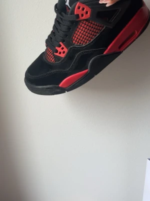 Svarta och röda sneakers med meshdetaljer - Säljer ett par svarta Jordan 4s sneakers med röda detaljer. Storlek 38.Pris kan diskuteras.