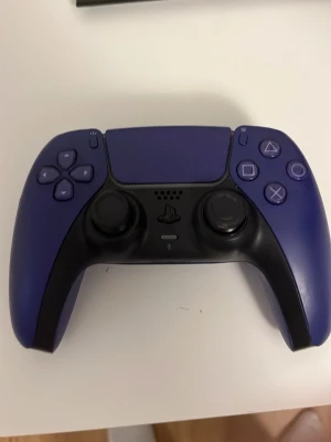 Lila PlayStation 5 DualSense handkontroll - Snygg lila PlayStation 5 DualSense handkontroll med svart frontpanel och klassiska PlayStation-knappar. Ergonomisk design med greppvänliga handtag och responsiva triggers. Perfekt för gaming på PS5 och har touchpad samt inbyggd högtalare.