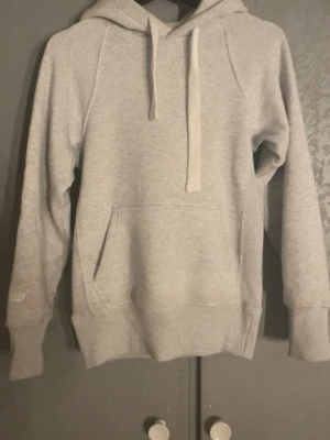 Russemerch hoodie  - En stilren ljusgrå hoodie med huva och dragsnören. Hoodien har en klassisk känguruficka framtill, ribbade muddar vid ärmslut och nederkant samt mjukt material som känns skönt mot huden. Perfekt för en avslappnad och trendig look.