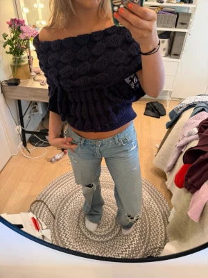 Mörkblå offshoulder stickad topp - Säljer en mörkblå, croppad offshoulder topp i stickat material. Toppen har ett bubbligt mönster och sitter löst över axlarna för en avslappnad vibe. Perfekt för dig som vill ha något unikt och trendigt i garderoben.