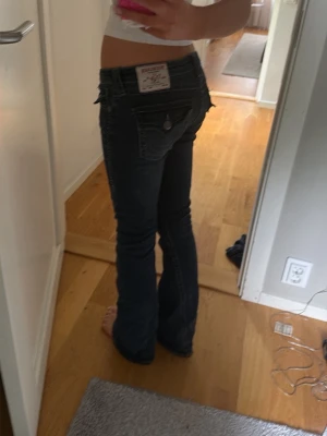 Mörkblå bootcut jeans med broderi och glitterstenar - Säljer ett par mörkblå bootcut jeans med snygga broderade detaljer på bakfickorna och kontrastsömmar. Dessutom små glitterstenar. Jeansen har låg midja och klassisk femficksdesign. Perfekta för dig som gillar en avslappnad men ändå trendig look.