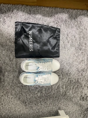Blåvita sneakers från Numeris(PRIS GÅR ATT DISKUTERA) - Snygga sneakers från Numeris i vitt och ljusblått med mönstrad textil på sidorna och vita detaljer på tå, snörning och sula. Klassisk låg modell med tjock sula och stilren design. Perfekta för dig som vill ha något unikt och trendigt.