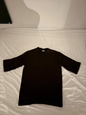 Svart t-shirt med trekvartsärm - En stilren brun  tröja  med trekvartsärm och rund hals. Modellen är rak och har en lite längre passform, perfekt för en avslappnad look. Tillverkad i mjukt material som känns skönt mot huden.