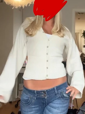 Vit ribbad kofta med knappar - Snygg vit kofta med ribbad midja och v-ringning. Koftan har långa, lite vidare ärmar och stängs med knappar framtill. Perfekt att styla med jeans för en avslappnad look.