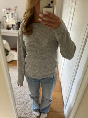 Ljusgrå stickad tröja från H&M - En enkel och stilren ljusgrå stickad tröja från H&M. Tröjan har rund halsringning, långa ärmar och ribbade muddar vid ärmslut och nederkant. Perfekt att matcha med jeans för en avslappnad look.
