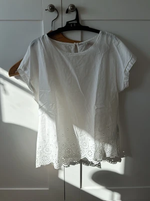 Vit blus från Jacqueline de Yong - Söt vit blus från Jacqueline de Yong med broderade detaljer och hålmönster längst ner samt en liten knapp i nacken. Den har en pytteliten ljusrosa fläck (se bild 6), men går nog bort i tvätten🧡