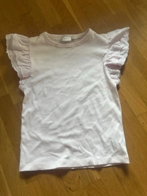 Ljusrosa topp med volangärmar - Supersöt ljusrosa topp med volangärmar i broderad spets. Toppen har rund halsringning och är tillverkad i mjuk bomull, perfekt för en söt och feminin look. Volangdetaljerna ger en extra touch till outfiten. Aldrig använts men finns tyvärr ingen prislapp kvar. 