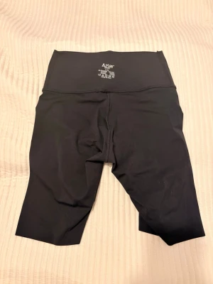 Svarta cykelshorts från ARIAE - Säljer ett par svarta cykelshorts från ariae med hög midja och stretchigt material. De har en diskret logga framtill och är perfekta för träning eller chill. Materialet känns mjukt och följsamt, och längden går till strax ovanför knät. Aldrig använda då det var lite små för mig. 