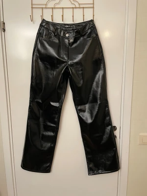 Snygga glansiga byxor från FB Sister, stl M - Säljer ett par svarta glansiga jeans från FB Sister i storlek M. Byxorna har raka ben, hög midja och klassisk femficksmodell. Materialet är konstläder som ger en cool och trendig look. Perfekta för dig som vill sticka ut lite extra.