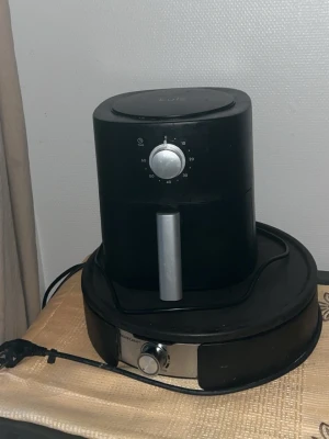 Svart airfryer och robotdammsugare - Säljer en svart airfryer med silverfärgad ratt och handtag samt en svart robotdammsugare med silverdetaljer. Perfekt för dig som vill laga mat utan olja och samtidigt hålla golvet rent. Båda har sladd och enkel design.