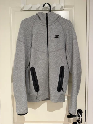 Grå Nike hoodie med dragkedja - Pris går alltid o diskutera. Snygg grå hoodie från Nike med hel dragkedja framtill och svarta detaljer på fickorna. Klassisk huva och Nike-logga på bröstet. Tillverkad i mjukt sweatshirtmaterial, perfekt för chill eller träning.