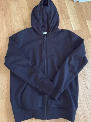 Svart zip-hoodie med dragkedja Kappahl - En svart zip-hoodie från Kappahl. Mjuk och go insida. Klassisk huva och ribbade muddar vid ärmar och nederkant. Mycket sparsamt använd. Bara tvättad en gång.