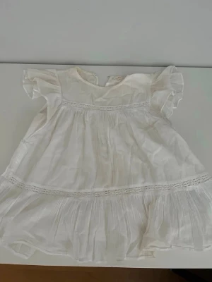 Vit blus med volang från Gina Tricot - Söt vit blus från Gina Tricot i luftig bomull. Blusen har volangdetaljer vid ärmarna och nertill, samt en liten öppning vid halsen. Perfekt för en fräsch och somrig look.