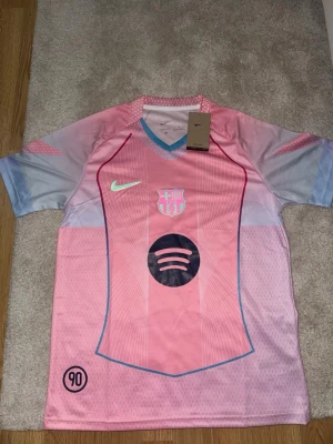 Rosa FC Barcelona tröja - Säljer en rosa FC Barcelona matchtröja från Nike med ljusblå och lila detaljer. Tröjan har klubbmärke, Nike-logga och Spotify som sponsortryck på bröstet. Tillverkad i ett lätt och ventilerande material, perfekt för fotbollsträning eller match. Säljer den för det passar tyvärr inte så tänker köpa en ny och sälja denna. Kan sänka priset vid snabb affär 