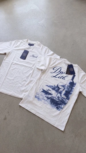 Vit t-shirt med blått tryck - Säljer en vit t-shirt med blått tryck på ryggen och diskret text på bröstet. T-shirten har klassisk passform och korta ärmar. Perfekt för dig som gillar stilrena plagg med en twist.