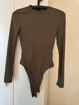 Brun långärmad body från SHEIN - Säljer en enkel och stilren brun body från SHEIN i storlek S. Bodyn har långa ärmar, rund halsringning och är tillverkad i ett stretchigt, mjukt material som sitter tight mot kroppen. Perfekt att matcha med jeans eller kjol.