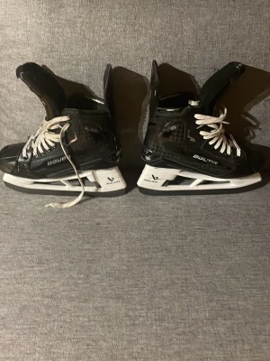 Bauer Supreme mach skridskor stl,6,5 - Säljer ett par svarta Bauer Supreme hockeyskridskor med vita snören och vita sulor. Skridskorna har en modern design med detaljer i silver och svart, samt robust plastmaterial och skyddad häl. Perfekta för isträning eller match. Dem är också custom gjorda från Bauer.