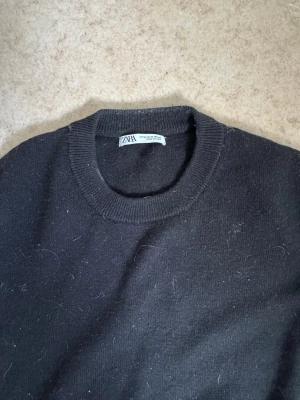 Svart stickad tröja från Zara i ull - En enkel och stilren svart stickad tröja från Zara i ull med rund halsringning och ribbade muddar vid ärmslut och nederkant. Perfekt för lager-på-lager och passar till många olika outfits. Materialet är mjukt och bekvämt. Säljs för 200kr. Kontakta mig om du har frågor eller vill lägga bud.