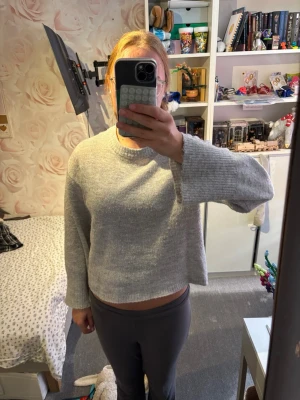 Ljusgrå stickad tröja med rund hals - Mysig ljusgrå stickad tröja med rund hals och långa ärmar. Tröjan har en rak, något boxig passform och är stickad i ett mjukt material som känns skönt mot huden. Perfekt att slänga på sig när det är kyligt ute.