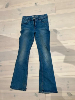 Blå flare jeans från Blue Ridge - Snygga blå jeans med utsvängda ben från Blue Ridge. Modellen är flare och har klassisk femficksdesign, dragkedja och knapp framtill. Jeansen har en cool tvättad look och passar perfekt till en trendig vardagsstil.