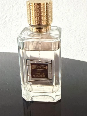 Ex Nihilo Lust in Paradise parfym - Ex Nihilo Lust in Paradise är en exklusiv parfym i en elegant, genomskinlig glasflaska med guldigt lock och detaljer. Flaskan har en stilren, fyrkantig form och etiketten är svart och guld. Perfekt för dig som gillar lyxiga och unika dofter.