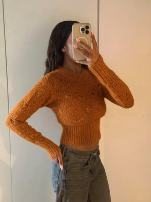  Ull/mohair tröja - Orange stickad tröja med cropped passform och långa ärmar. Tröjan har ett grovt stickat mönster och bred ribbad mudd vid midjan och ärmsluten. Perfekt till höstlooken och superenkel att styla med jeans.