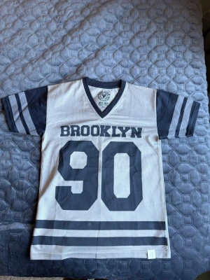 T-shirt fotbollströja - Football jersey med Brooklyn 90 på framsidan. Tröjan är grå och svart och gjord i ihåligt luftigt tyg