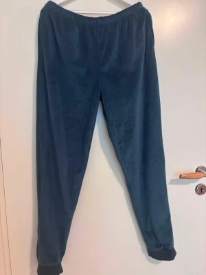 Mörkblå mjukisbyxor i fleece - Mörkblå mjukisbyxor med resår i midjan och muddar vid bensluten. Tillverkade i mjuk fleece som känns riktigt skön mot huden. Perfekta för chill dagar hemma eller när du vill vara extra bekväm.