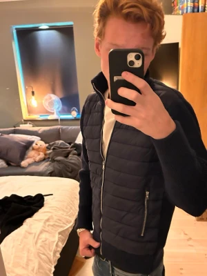 Leon Marcél Cardigan  - Säljer en helt ny snygg Marinblå Cardigan med quiltad front och stickade ärmar i storlek S. Jackan har hög krage, dragkedja framtill och två fickor med dragkedja. Perfekt för kyliga dagar och ger en modern look. Nypris ca 1300