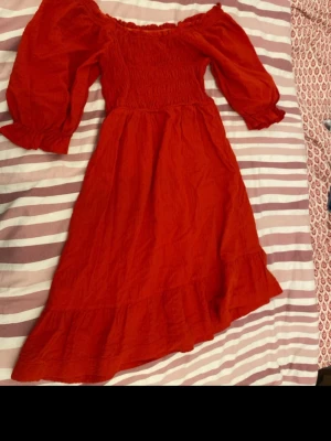 Röd långklänning med volang - Snygg röd långklänning med puffiga långärmar och smockad överdel. Klänningen har volangkant nertill och en söt, romantisk look. Perfekt för dig som vill sticka ut med färg och stil. Tillverkad i ett lätt tyg som känns skönt mot huden. Använts endast en gån på skolavslutningen. Köpt för 599kr. Säljer för 150kr