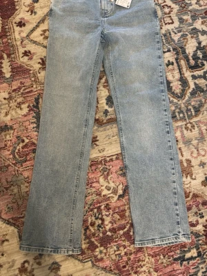 Ljusblå raka jeans - Säljer ett par ljusblå jeans med rak passform och klassisk femficksdesign. Jeansen har hög midja och är tillverkade i ett slitstarkt denimtyg. Perfekta för en avslappnad och trendig look.