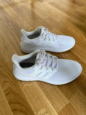 Vita Adidas skor  - Snygga helvita sneakers med ovandel i mesh och detaljer i syntet. Skorna har klassisk snörning och låg profil som ger en sportig look. Perfekta för dig som gillar stilrena och fräscha sneakers till vardags. Sulan är vit och ger bra komfort.