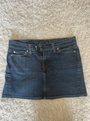Mörkblå jeanskjol från Crocker - Säljer en klassisk mörkblå jeanskjol från Crocker. Kjolen har fem fickor, bälteshällor och stängs med dragkedja och knapp framtill. Materialet är slitstarkt denim och modellen är rak och kort. Perfekt för dig som gillar en tidlös och enkel stil.