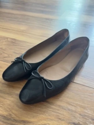 Svarta ballerinaskor från Flattered - Stilrena svarta ballerinaskor med rundad tå och en söt liten rosett framtill. Äkta läder! Använda 2 gånger. Nypris: 2 300kr. Hör av er vid frågor!