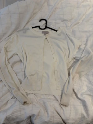 Vit kofta från H&M, storlek S - Säljer en klassisk vit kofta från H&M i storlek S. Koftan har rund hals, långa ärmar och knappar framtill. Ribbstickade muddar vid ärmslut och nederkant. Perfekt att slänga över en topp för en enkel och clean look.