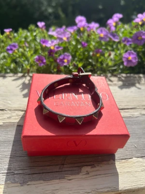 Valentino Garavani armband  - Snyggt armband från Valentino i rött läder med guldfärgade pyramidformade nitar. Justerbart spänne för perfekt passform. Kommer i original ask och med tygpåse. Perfekt accessoar för att lyfta din outfit.