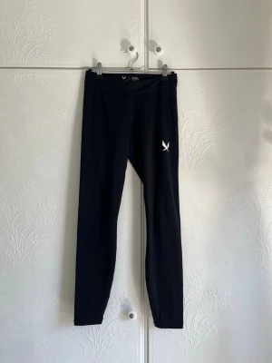 Svarta träningstights från SOC - Svarta träningstights från SOC i stretchigt funktionsmaterial. Midwaisted och diskret logga på benet. Perfekta för gym, löpning eller annan träning där du vill ha bra rörelsefrihet och en tight passform.