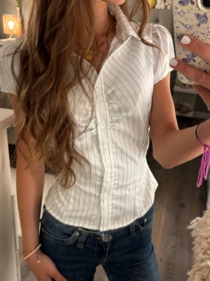 Vit randig skjorta med kort ärm - Snygg vit randig skjorta med kort ärm och knyt baktill som markerar midjan vilket ger en väldigt fin passform⭐️💕 oanvänd