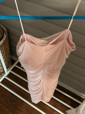 Ljusrosa glittrig kort klänning - Supersöt ljusrosa kort klänning med tunna axelband och glittriga detaljer. Klänningen har rynkade sömmar framtill som ger en snygg form och är perfekt för dig som vill sticka ut lite extra.